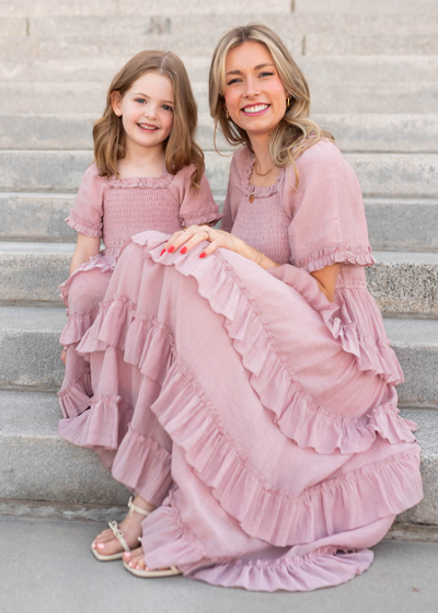 Woman and young girl in matching pink ruffled Tiered dresses sitting on steps.