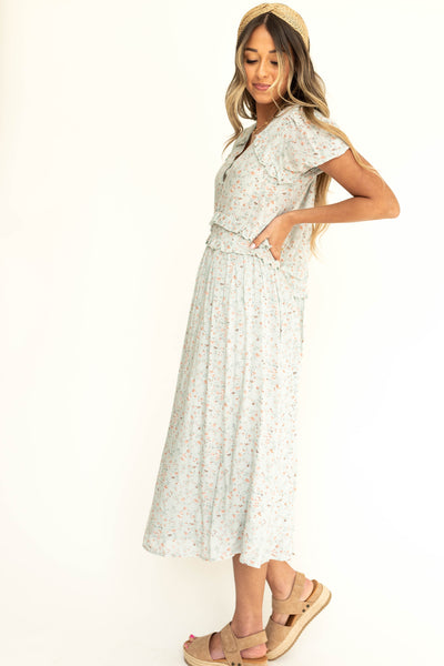 Side view of a light seafoam short sleeve floral dress with ruffle at sleeve.