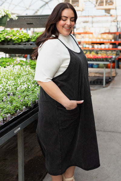 Side view of a plus size black washed jumper dress with pockets