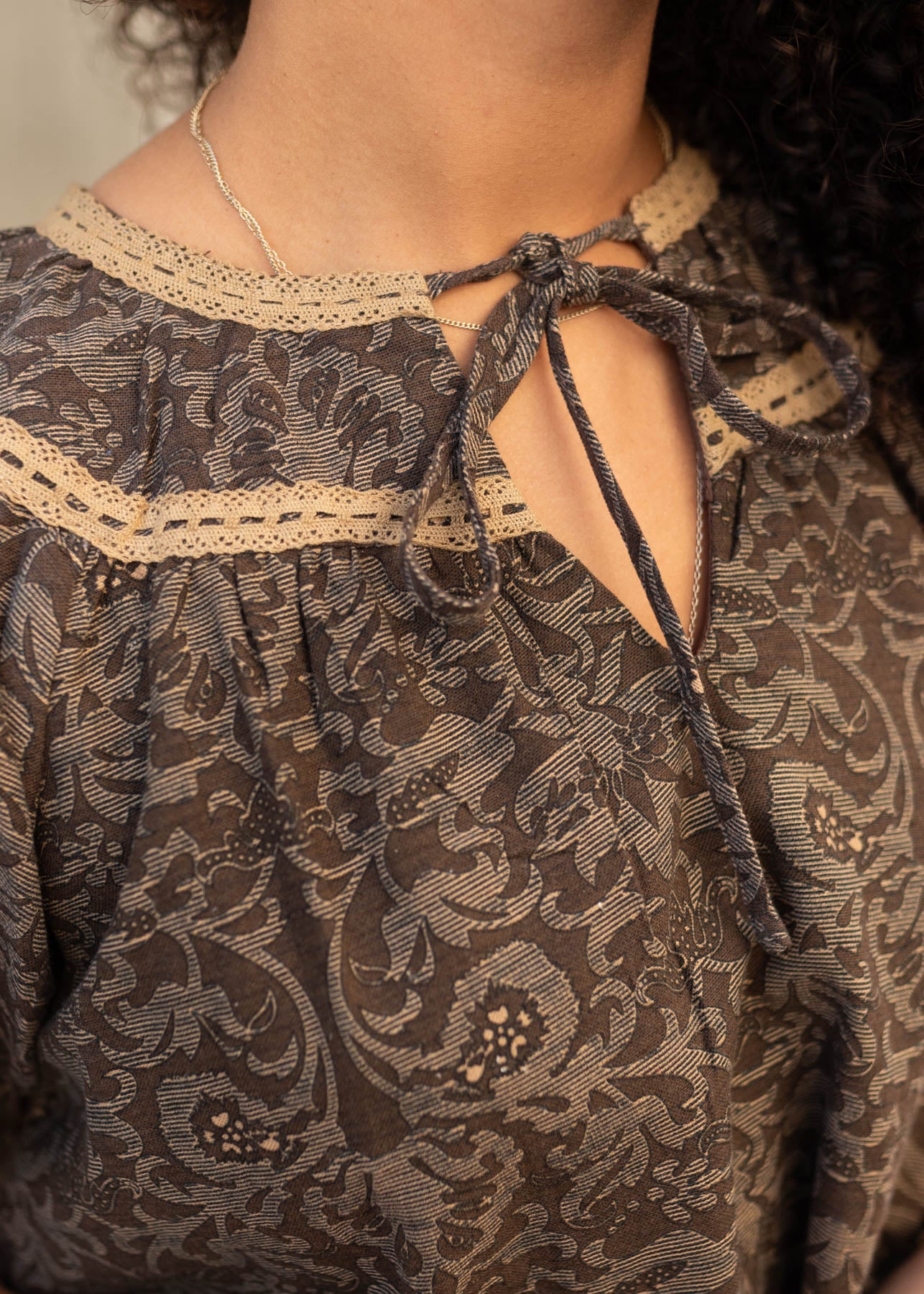 Close up of the fabric and gold trim on the brown pattern top with a tie at the neck.
