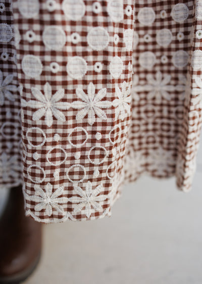Close up of the embroidery on the hem of the brown gingham dress