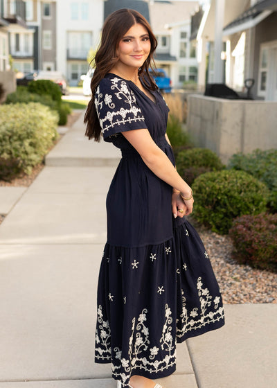 Side view of the navy embroidered dress with embroidery on the the sleeves and hem