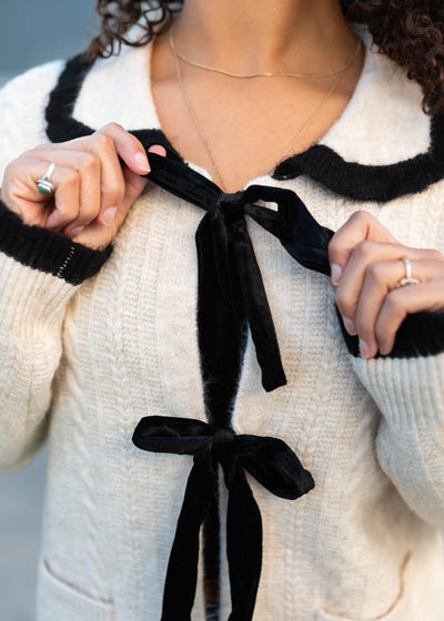 Cream bow cardigan with a close up of the black bows and black trim